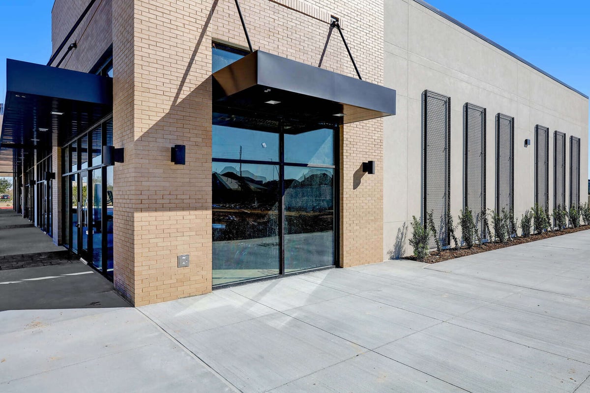 Glass entryway and brick façade of a modern commercial property with adjacent sidewalk in Houston, TX
